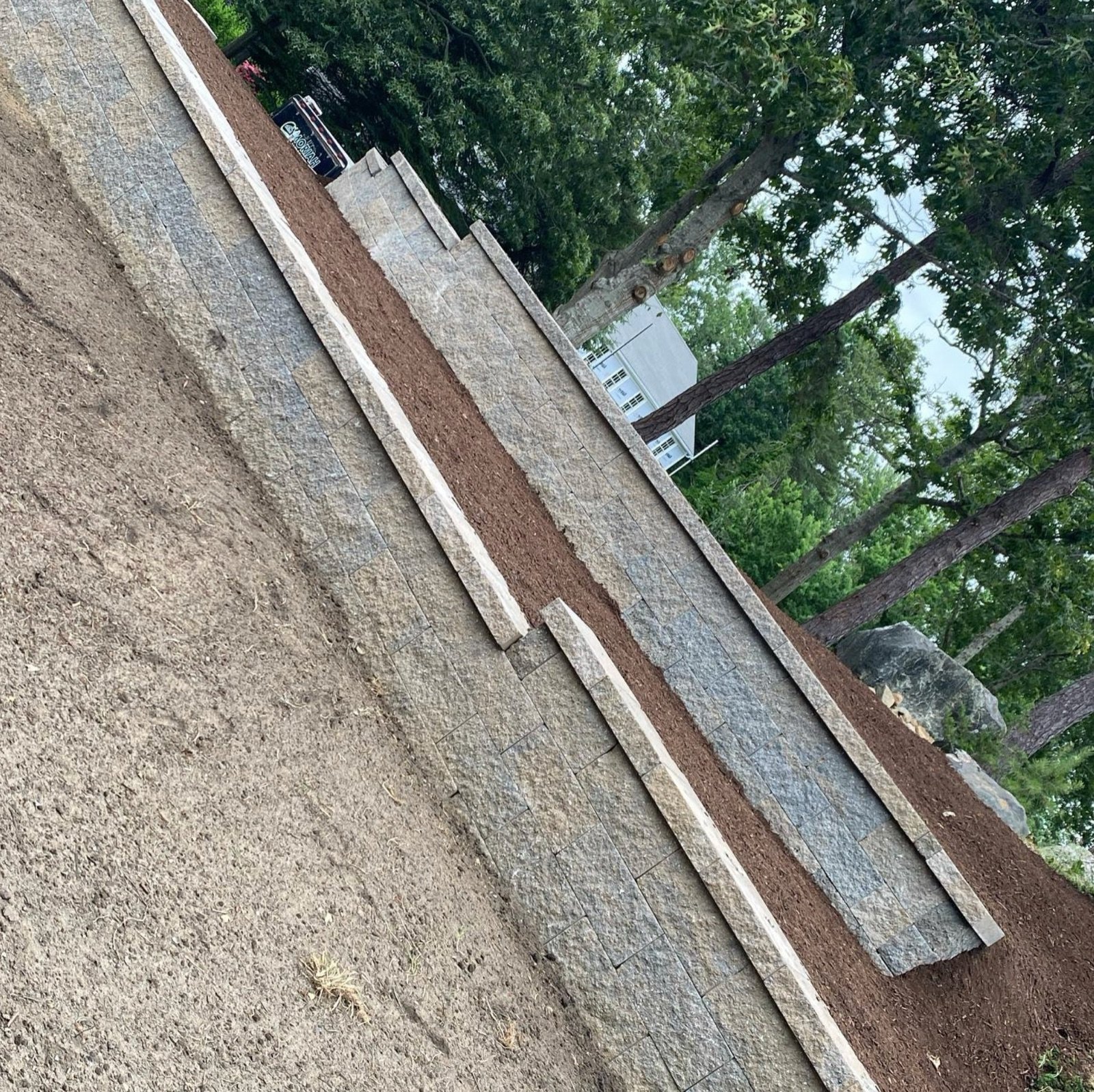 Block retaining wall with its cap course set, holding a raised bed above a driveway