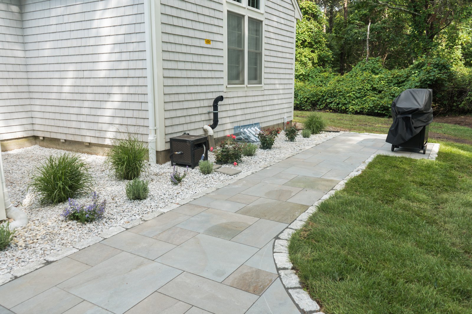 Bluestone walkway with a cobble edge running along the side of a Brewster home to the back lawn