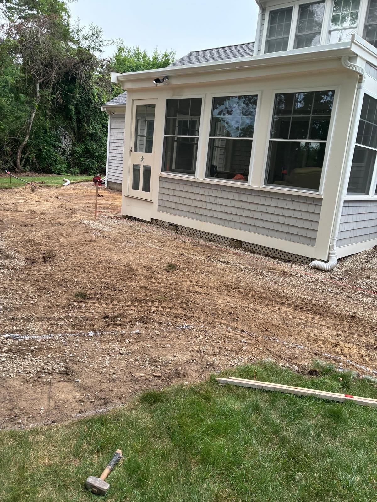 Bare graded soil and compacted base behind a Brewster home before the bluestone patio was set, July 2026