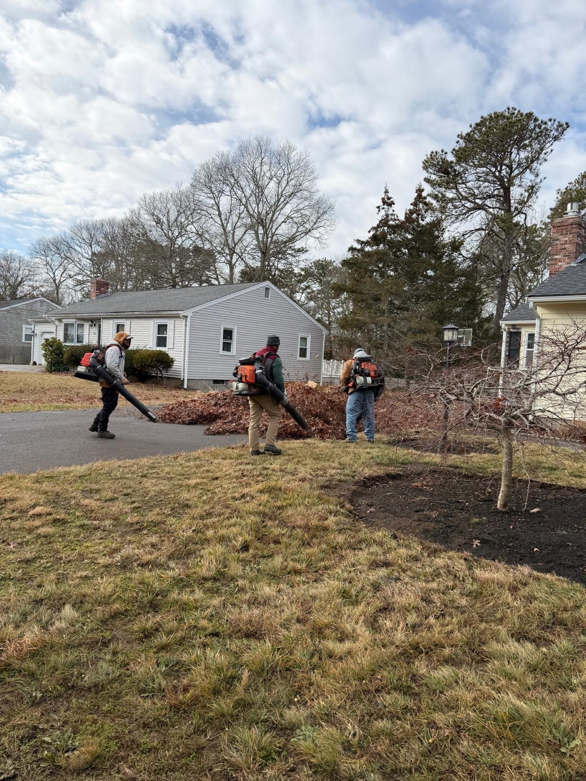 Three Moriah crew members clearing leaves with backpack blowers during a Cape Cod cleanup