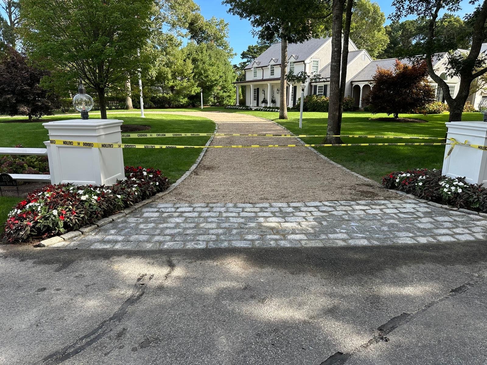 Cobblestone driveway apron meeting asphalt, with planted beds either side of the entry