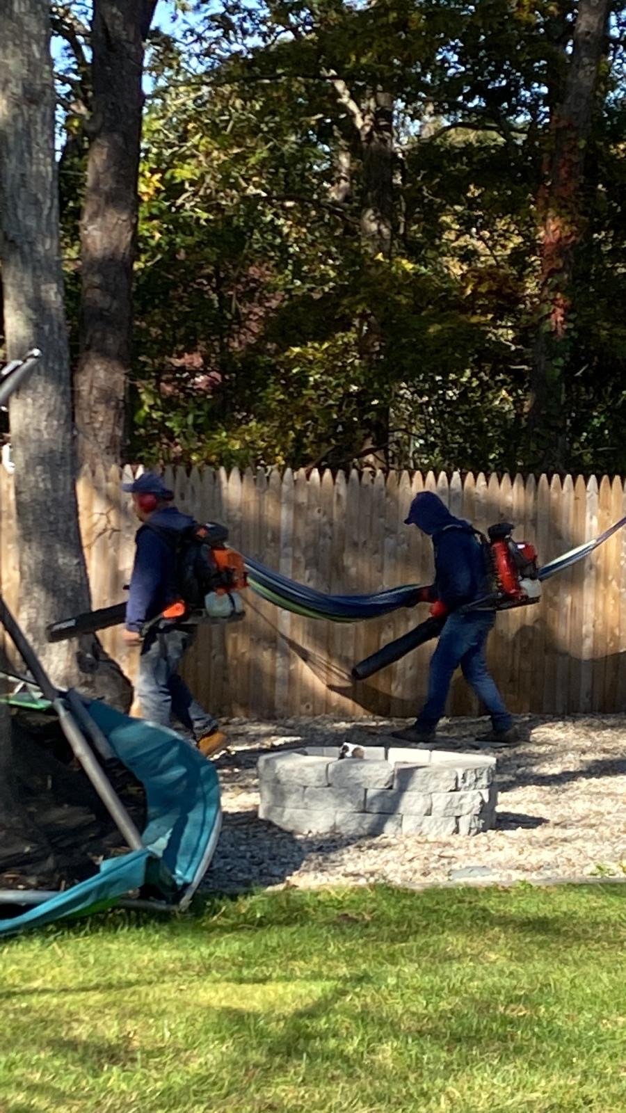 Two crew members clearing leaves with backpack blowers during a fall cleanup