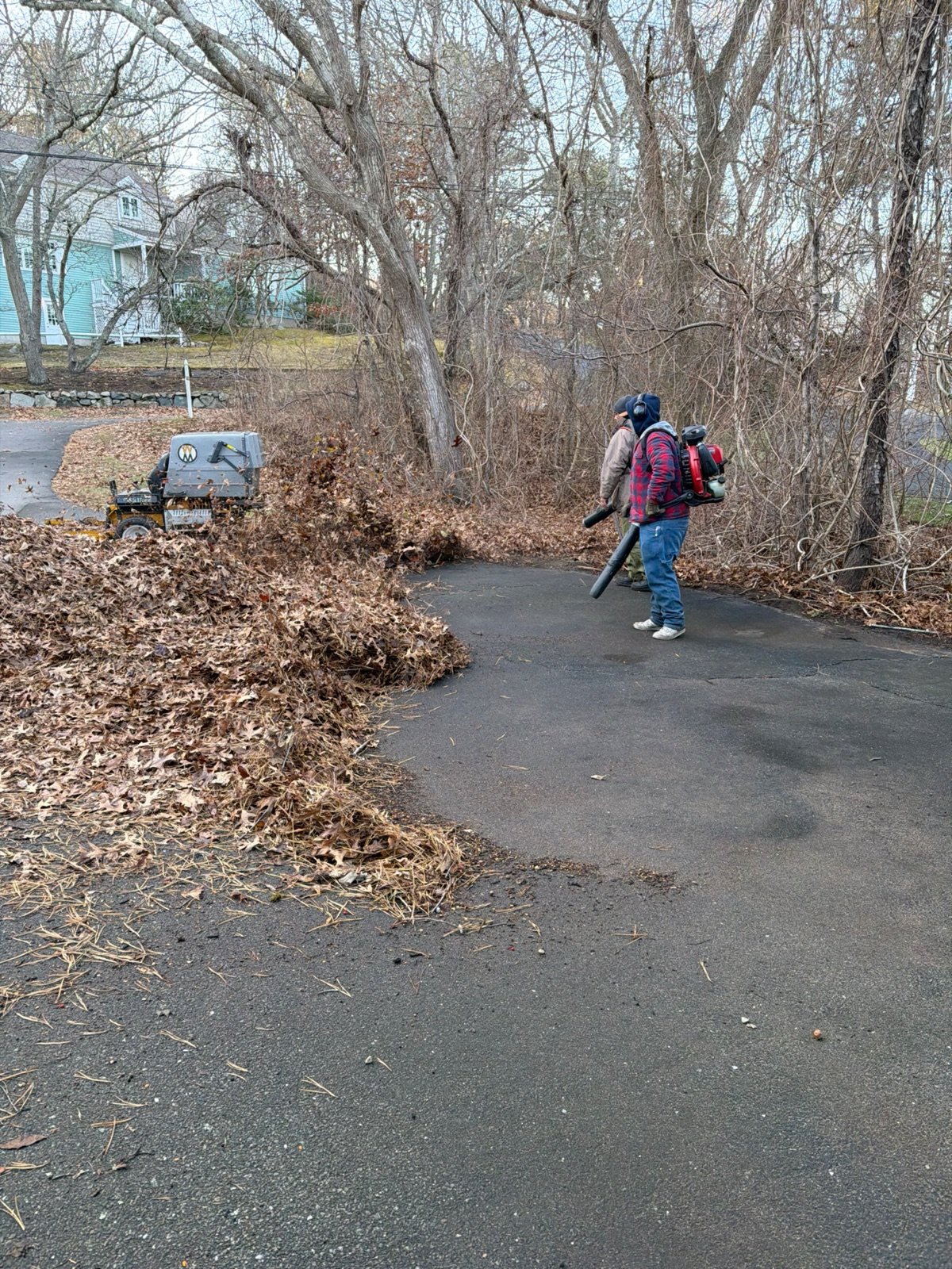 A crew member blowing leaves clear of a driveway edge during a fall cleanup