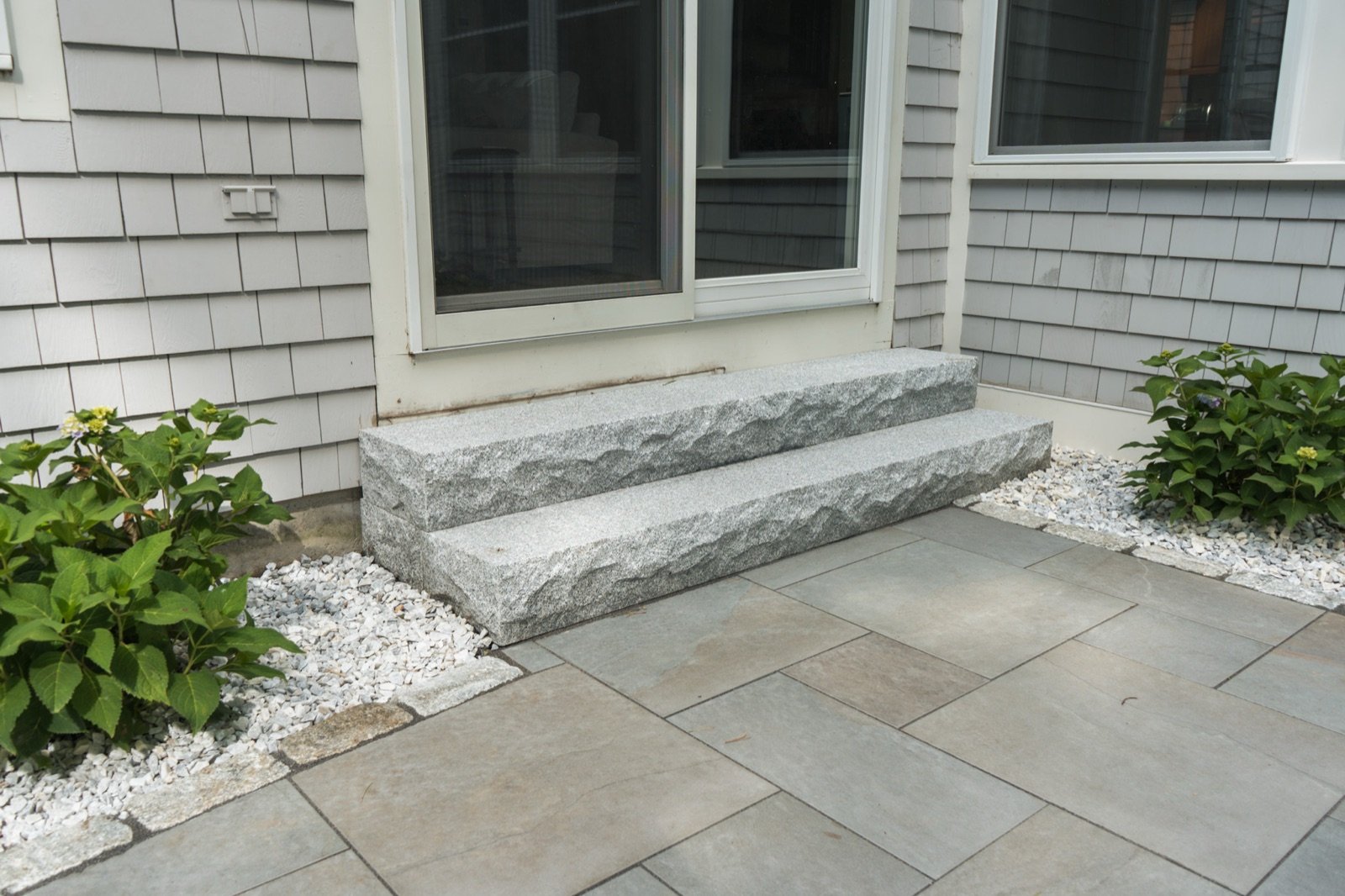 Granite step and bluestone landing forming the entry at a shingled house
