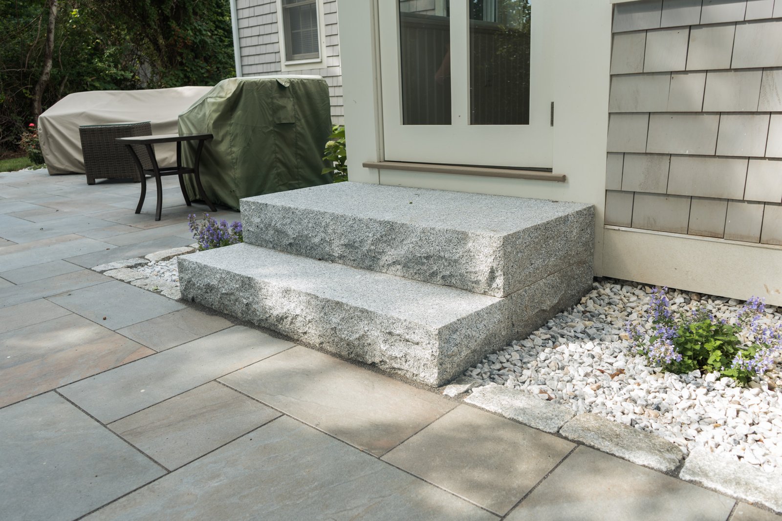 Granite block steps set into a bluestone patio beside a white stone planting bed in Brewster, MA