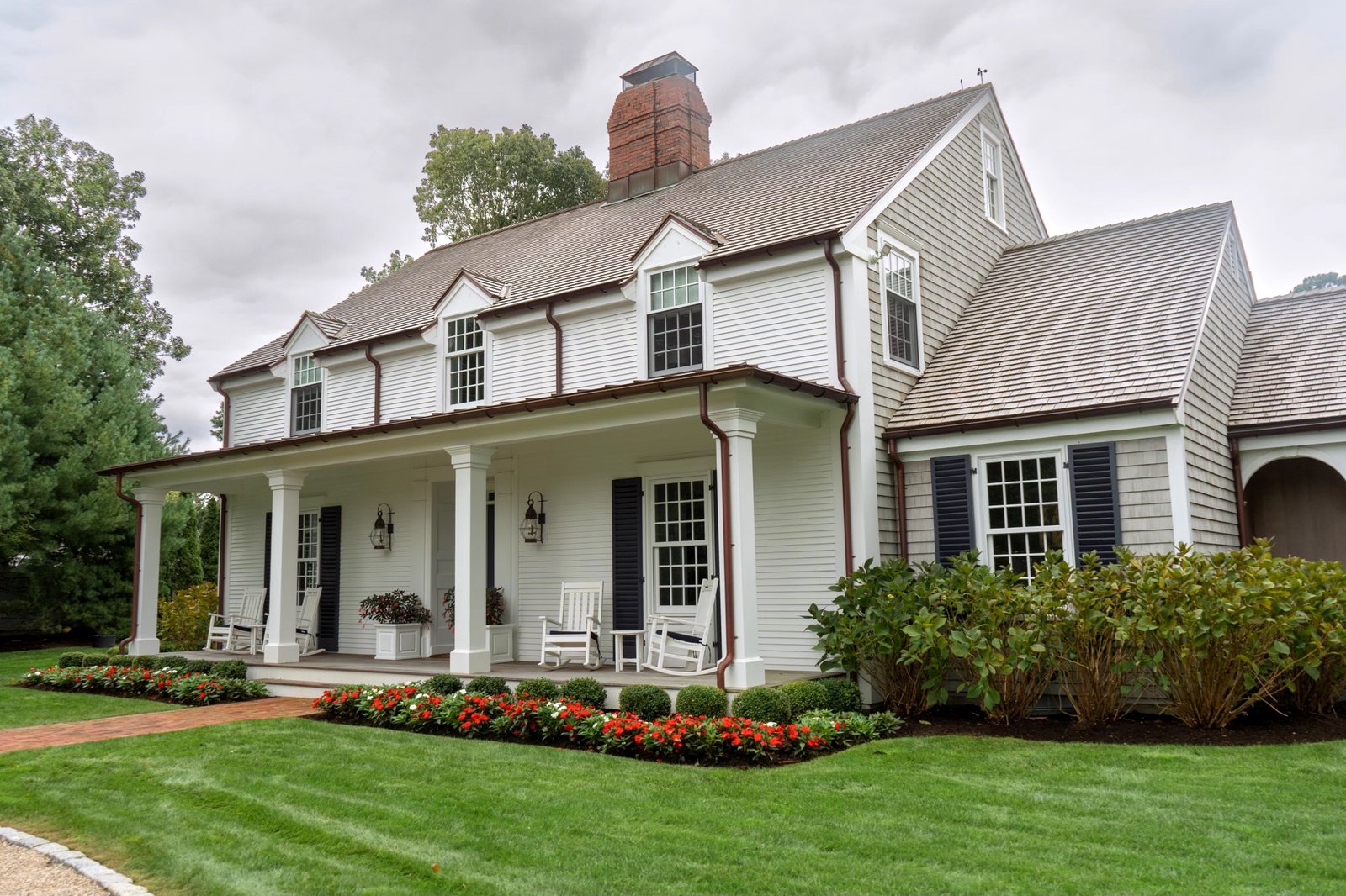 White colonial with planted borders and a mature hedge along the front of the property