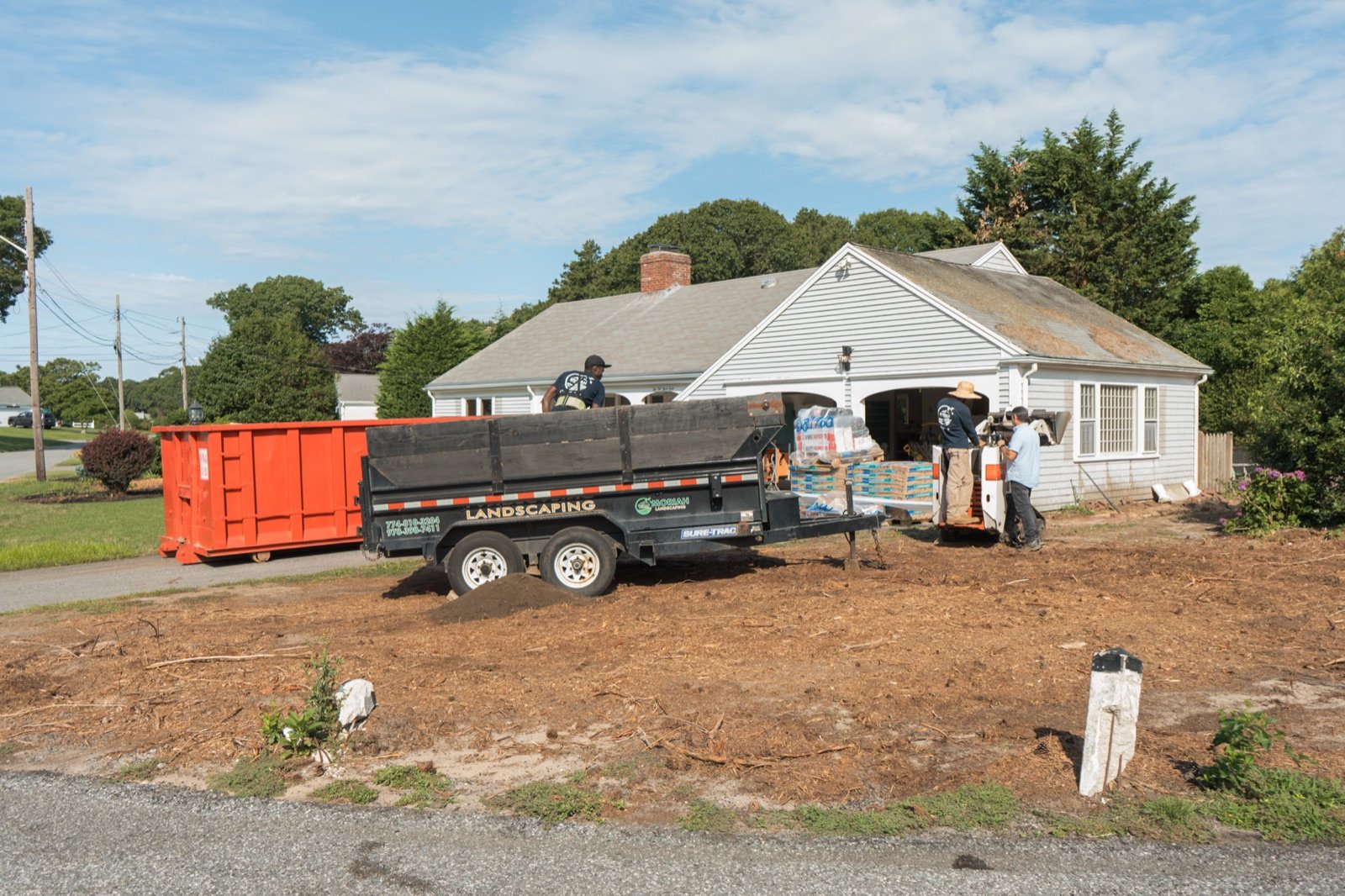 Site prep for a new patio, with the old surface stripped and spoil loaded for haul-off