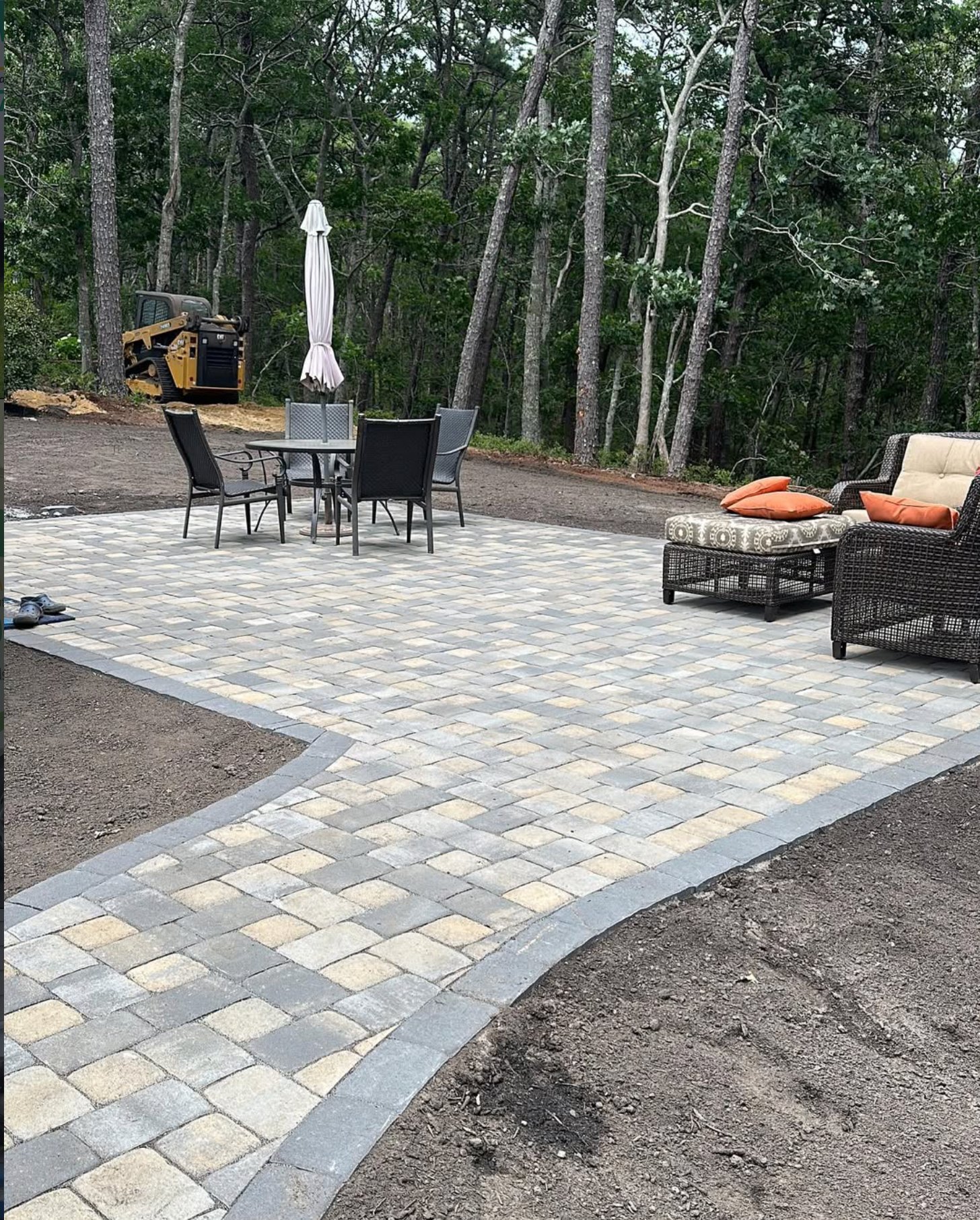 Curved paver patio with a contrasting border and outdoor furniture, newly installed on Cape Cod