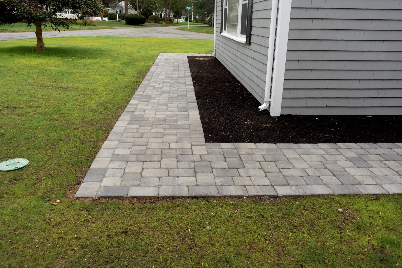 Paver patio turning the corner of a house, edged against a mulched planting bed