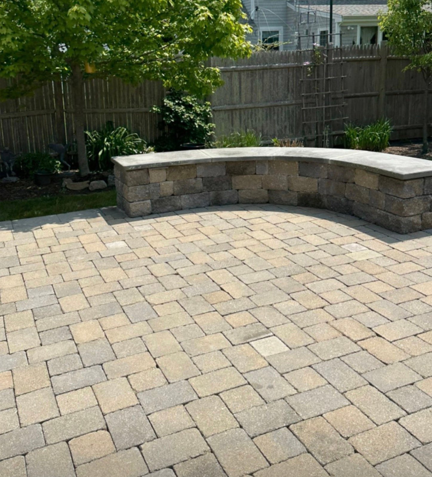 Paver patio with a curved seat wall enclosing the far edge of a back yard