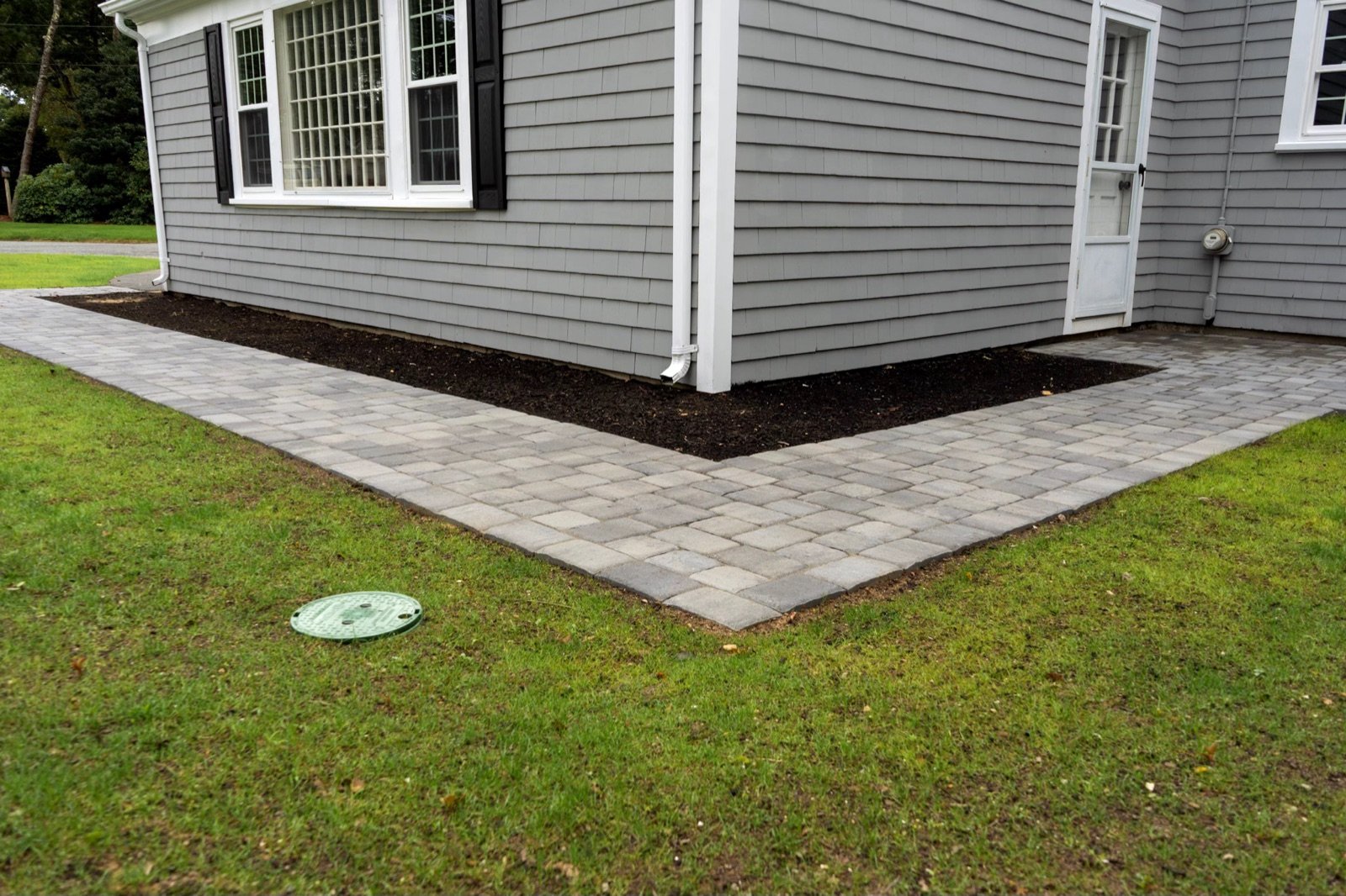 Paver patio running along a house wall to a mulched planting bed
