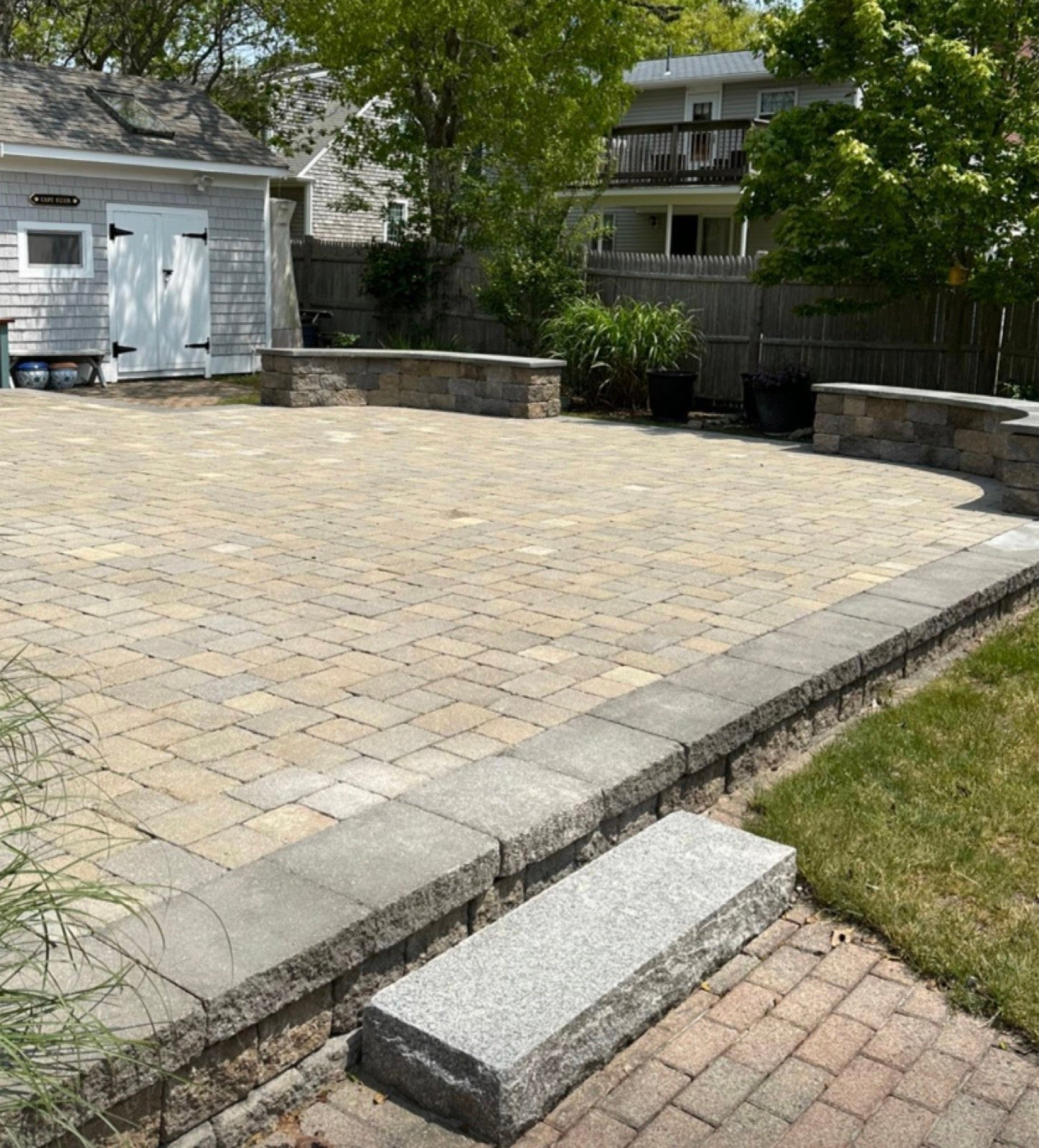 Large paver patio with a seat wall and granite step at a South Yarmouth home, built by Moriah Masonry & Landscaping