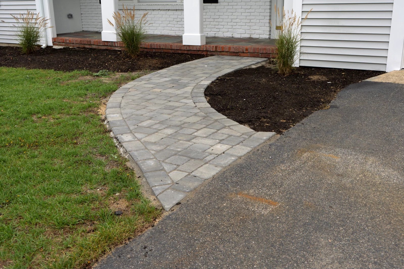 Paver walkway curving from a front door out to the driveway edge