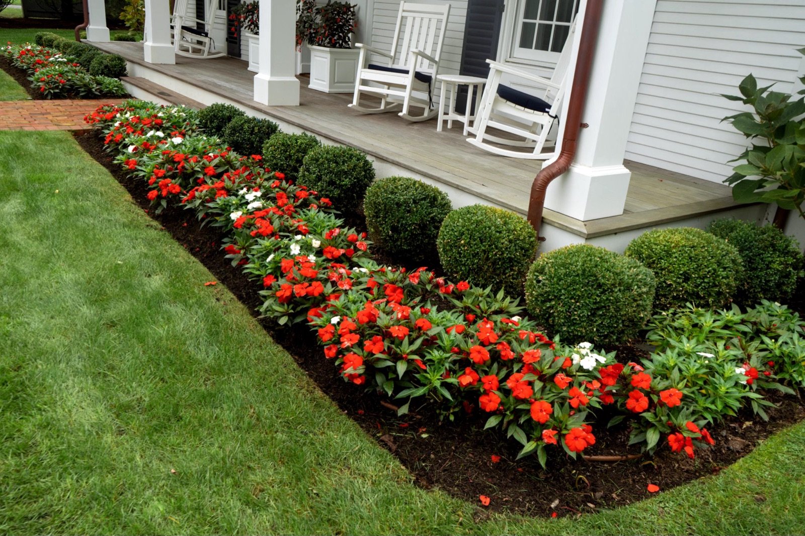 A planting bed of annuals and clipped shrubs running the length of a covered porch