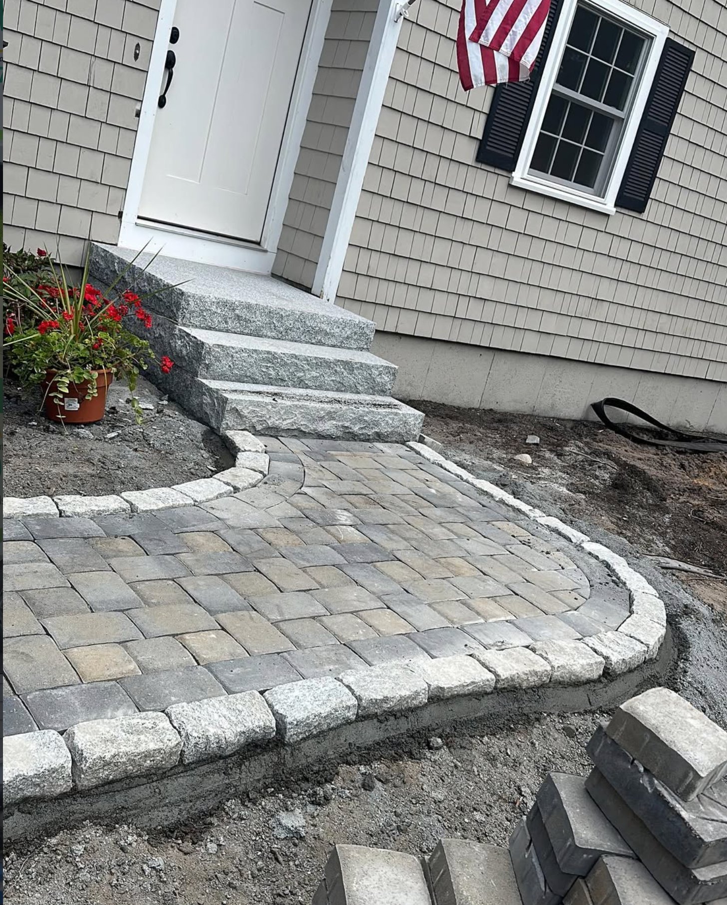 Granite block steps and a cobble-edged paver landing at the front door of a shingled Cape home